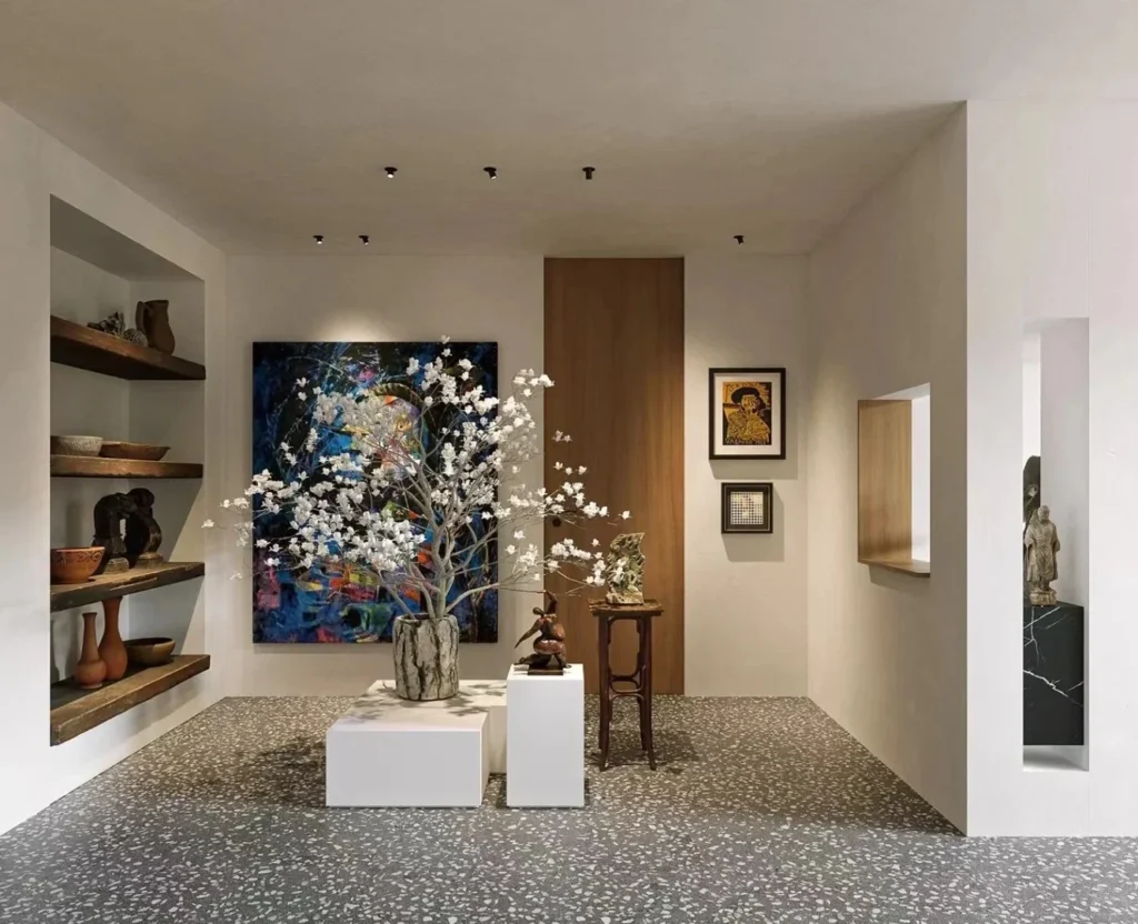 Terrazzo flooring in art gallery, wabi‑sabi modern interior, pottery display shelf, large floral installation, abstract painting, recessed spotlights