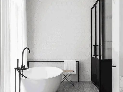 Dark terrazzo bathroom floor, black‑and‑white minimalist bath room, hexagon wall tiles, freestanding bathtub, black metal shower partition
