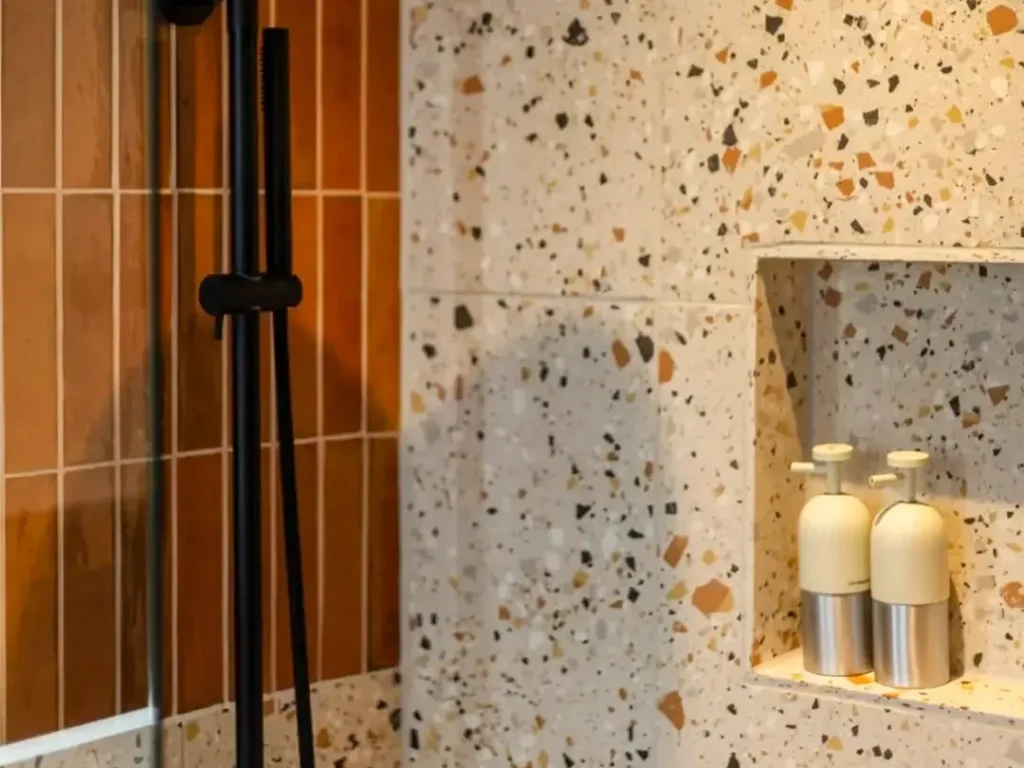 Piastrelle in terrazzo colori per piccole superfici: rivestimento in terrazzo con scaglie nere, arancioni e beige per bagno moderno con nicchia porta flaconi.