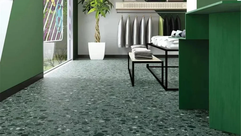 Come scegliere le piastrelle in terrazzo: variante a contrasto scuro — pavimento in terrazzo verde foresta con aggregati bianchi e grigi in un negozio di abbigliamento con pareti verdi, appendiabiti e pianta, ideale per contesti commerciali di grande impatto.